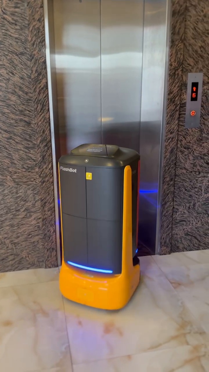 FlashBot Max chờ thang máy tại sảnh khách sạn